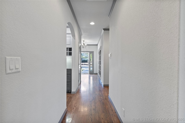 hall with arched walkways, dark wood-style flooring, a textured wall, and baseboards