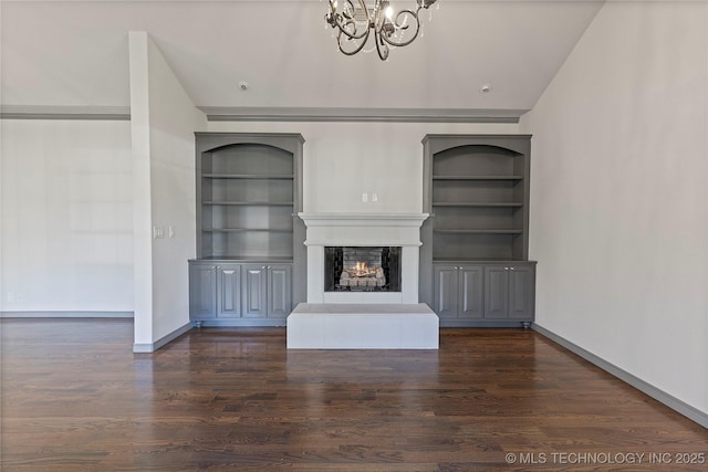 unfurnished living room with a warm lit fireplace, a chandelier, wood finished floors, baseboards, and built in features