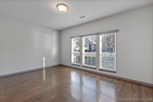 spare room with wood finished floors, visible vents, and baseboards