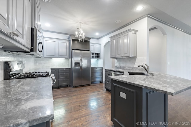 kitchen featuring arched walkways, a peninsula, a sink, appliances with stainless steel finishes, and dark wood finished floors