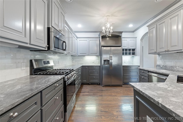 kitchen with decorative backsplash, light stone counters, appliances with stainless steel finishes, dark wood-type flooring, and gray cabinets