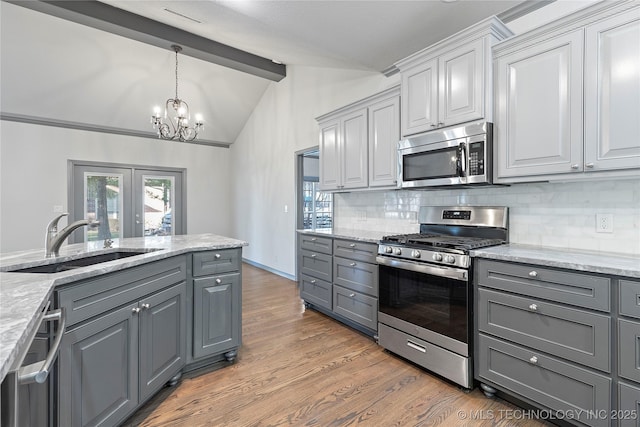 kitchen with lofted ceiling with beams, gray cabinetry, a sink, appliances with stainless steel finishes, and tasteful backsplash