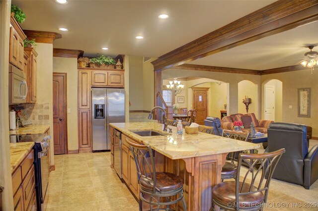 kitchen featuring arched walkways, a breakfast bar, a sink, open floor plan, and appliances with stainless steel finishes