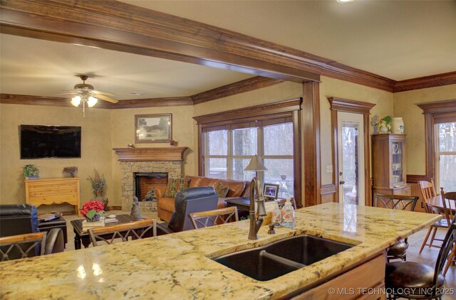 kitchen with crown molding, a fireplace, light stone counters, and a sink