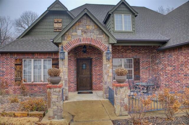 property entrance featuring stone siding, a shingled roof, and brick siding