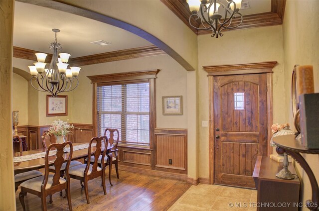 entrance foyer featuring a chandelier, arched walkways, wood finished floors, ornamental molding, and wainscoting