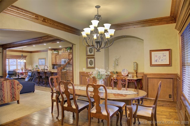 dining space featuring light wood-type flooring, arched walkways, a wainscoted wall, and an inviting chandelier