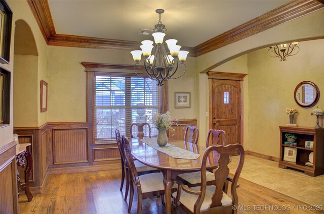 dining space featuring a wainscoted wall, arched walkways, a chandelier, and light wood finished floors