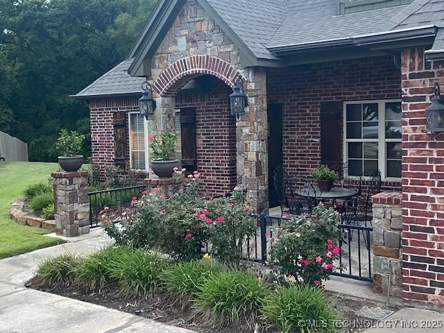 view of exterior entry featuring stone siding, a shingled roof, and brick siding