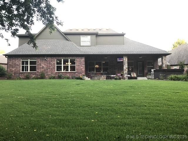 rear view of house with brick siding, a lawn, and roof with shingles