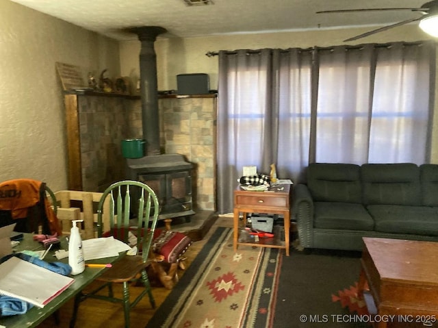 living room with a wood stove, ceiling fan, and a textured wall