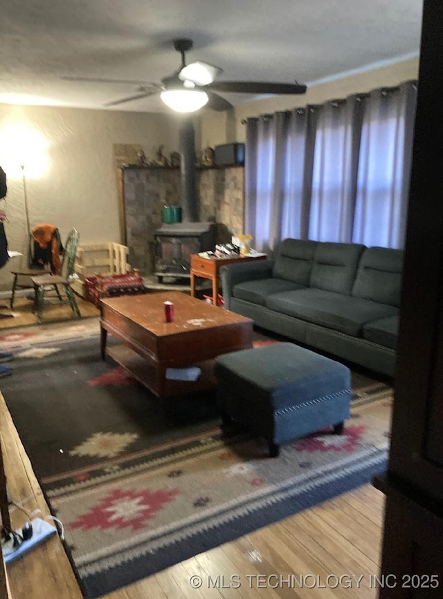 living room featuring a wood stove, a ceiling fan, and wood finished floors