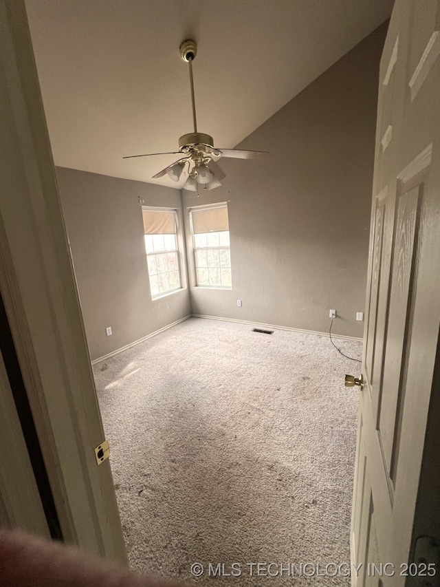 carpeted spare room with ceiling fan, vaulted ceiling, visible vents, and baseboards