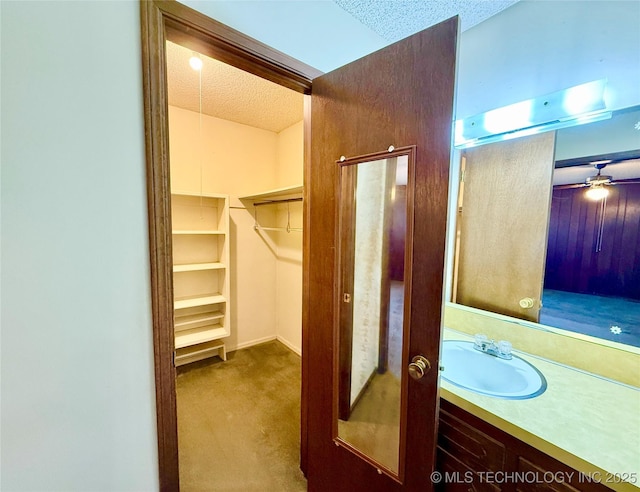 bathroom with a textured ceiling, a spacious closet, ceiling fan, and vanity