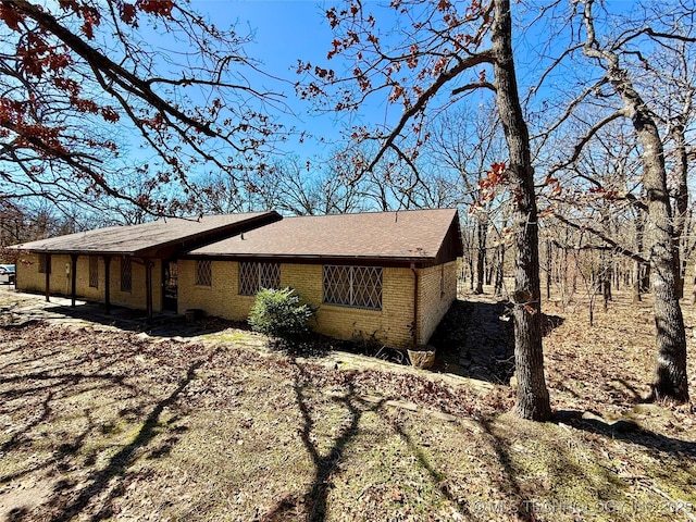 view of side of property with a shingled roof and brick siding