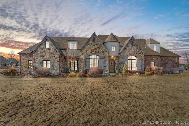 french provincial home featuring stone siding and a lawn