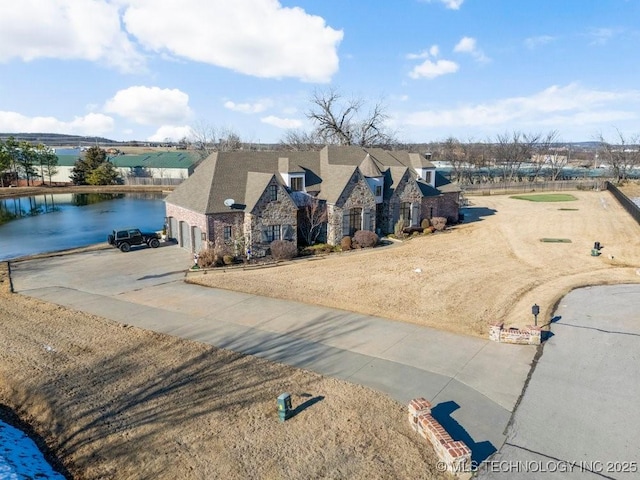 view of front of property featuring driveway, stone siding, and a water view