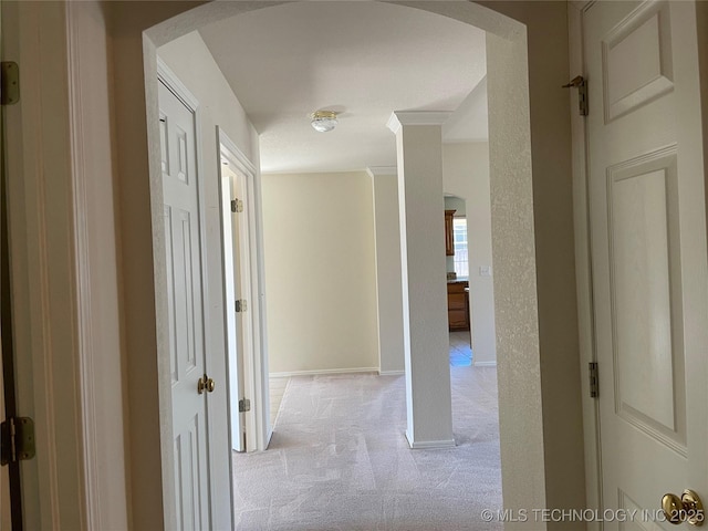 corridor featuring arched walkways, light colored carpet, and baseboards