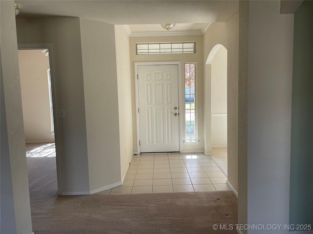 carpeted entryway with arched walkways, baseboards, tile patterned floors, and crown molding