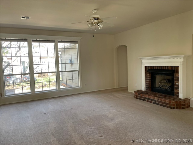 unfurnished living room featuring arched walkways, visible vents, ceiling fan, carpet flooring, and a fireplace