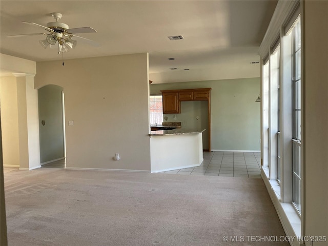 unfurnished living room featuring light carpet, visible vents, arched walkways, baseboards, and ceiling fan