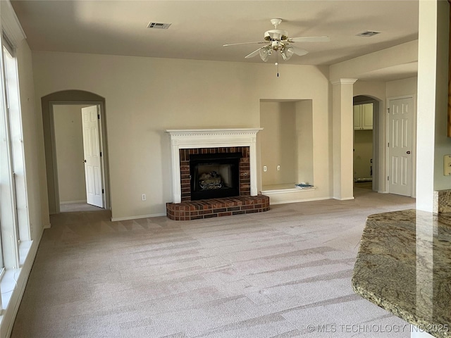 unfurnished living room featuring arched walkways, a fireplace, carpet flooring, and visible vents