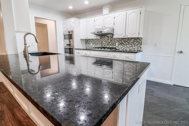 kitchen featuring tasteful backsplash, stainless steel appliances, under cabinet range hood, white cabinetry, and a sink