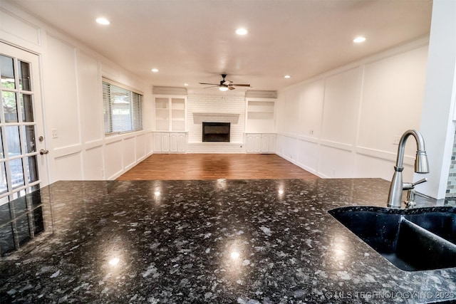 living area featuring a brick fireplace, ceiling fan, built in shelves, and a decorative wall