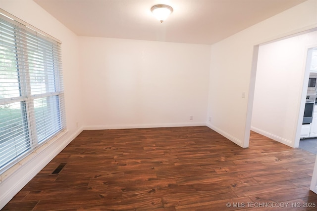 empty room featuring dark wood finished floors, visible vents, and baseboards