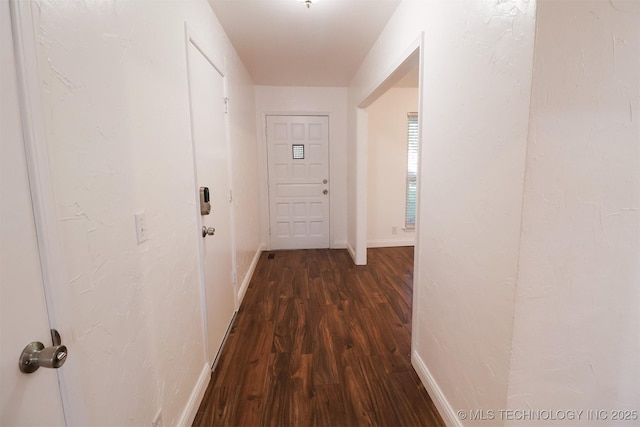 corridor featuring baseboards and dark wood-style flooring