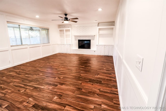 unfurnished living room featuring ceiling fan, a decorative wall, dark wood-type flooring, a fireplace, and built in features