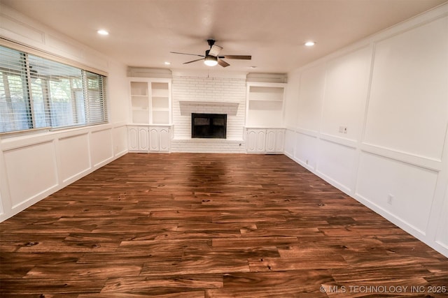 unfurnished living room with built in features, a decorative wall, and dark wood-style floors