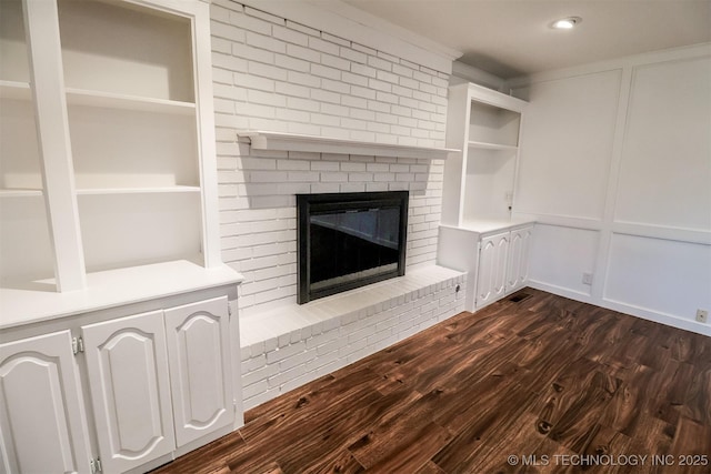 unfurnished living room featuring dark wood-type flooring, a brick fireplace, and a decorative wall