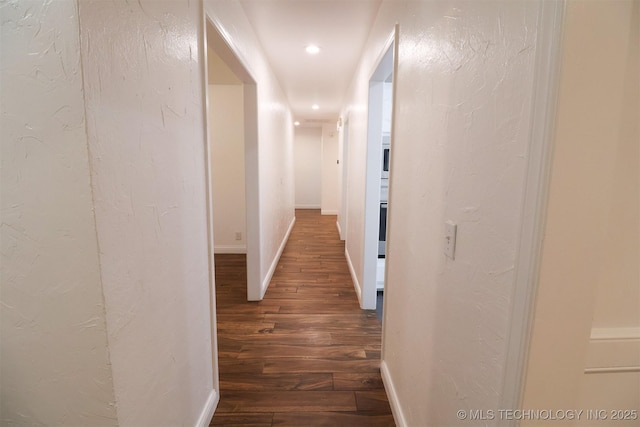 corridor with dark wood-type flooring, recessed lighting, a textured wall, and baseboards