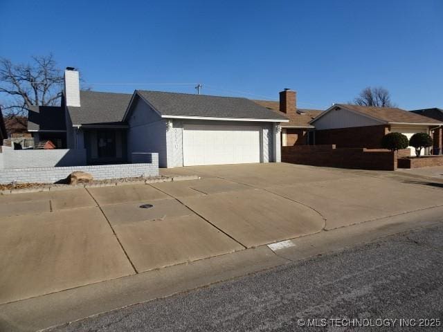 ranch-style home with driveway, an attached garage, and a chimney