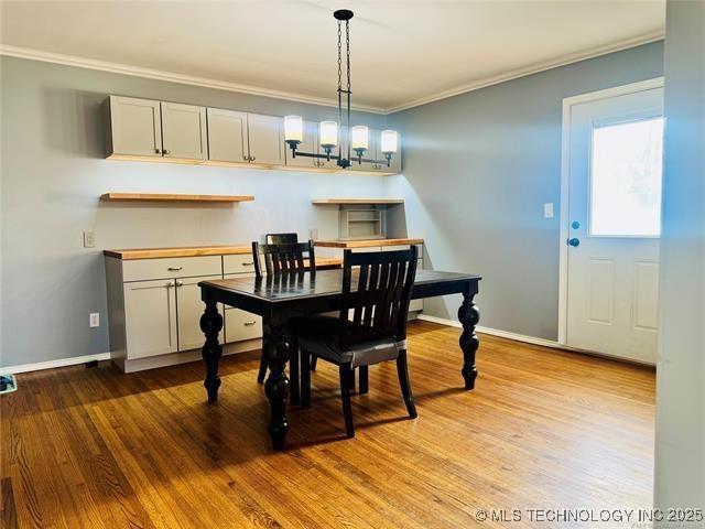 dining space with a chandelier, baseboards, wood finished floors, and crown molding