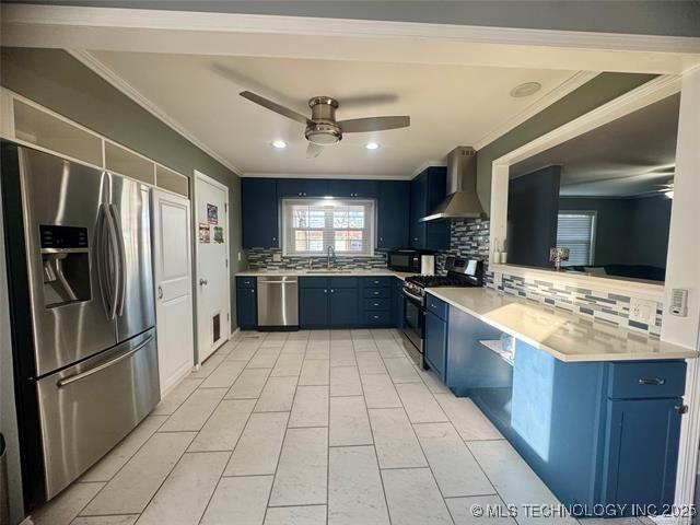 kitchen featuring ceiling fan, stainless steel appliances, light countertops, wall chimney range hood, and blue cabinetry