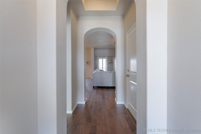 corridor with dark wood finished floors, baseboards, and arched walkways