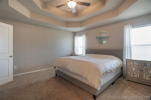 bedroom with visible vents, baseboards, a tray ceiling, carpet floors, and a ceiling fan