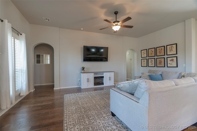 living area with a ceiling fan, visible vents, a fireplace, arched walkways, and dark wood-type flooring