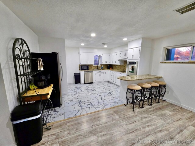 kitchen featuring visible vents, backsplash, a sink, a peninsula, and black appliances