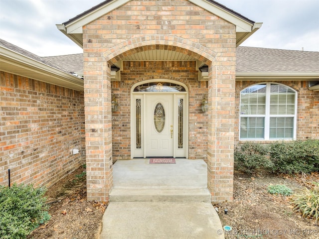 view of exterior entry with a shingled roof and brick siding