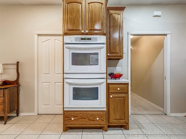 kitchen featuring baseboards, brown cabinetry, white double oven, light countertops, and light tile patterned flooring