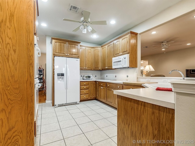 kitchen with light tile patterned flooring, a peninsula, white appliances, visible vents, and a ceiling fan