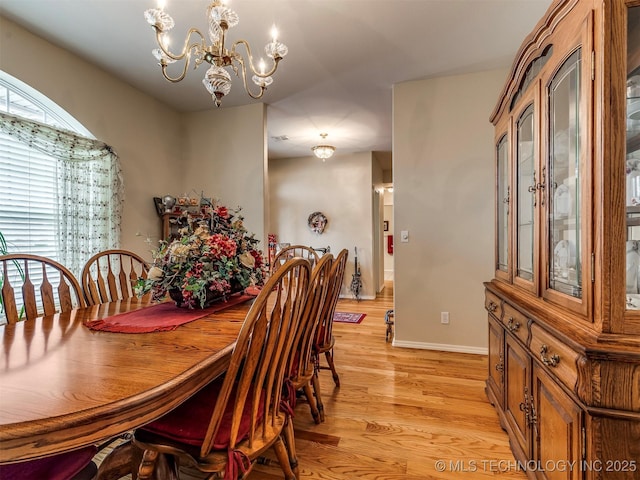 dining area with light wood-type flooring, baseboards, and a notable chandelier