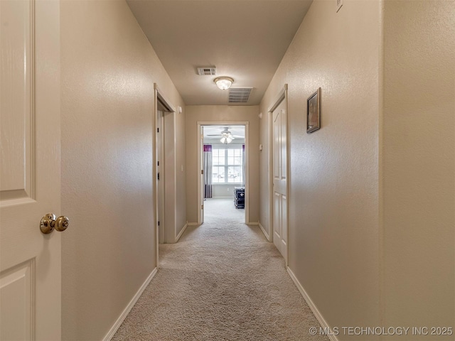 hallway with light colored carpet, visible vents, and baseboards