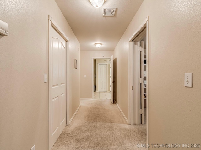 hall with light carpet, baseboards, and visible vents