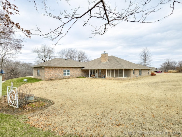 rear view of house featuring a sunroom, a chimney, and a yard