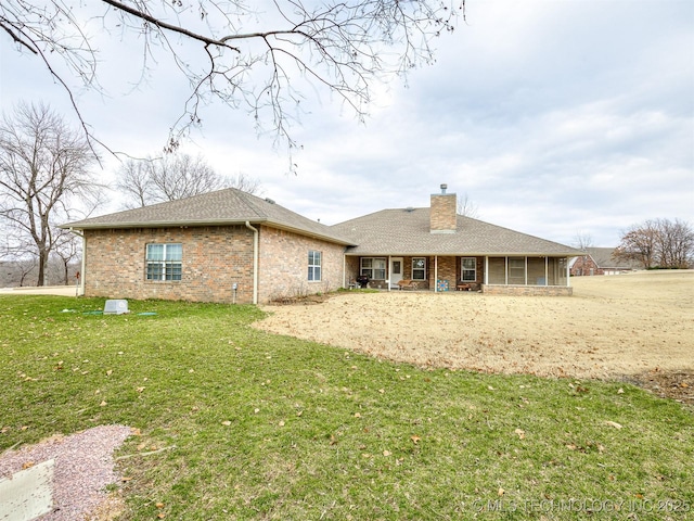 back of property featuring brick siding, a chimney, a shingled roof, a lawn, and a sunroom