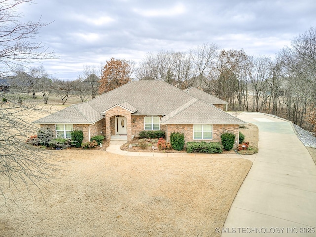 view of front of property featuring driveway, brick siding, and roof with shingles